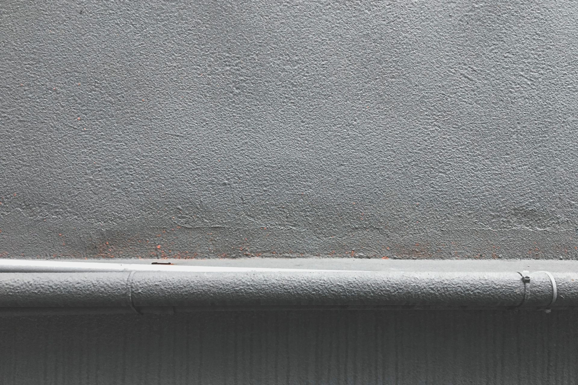 Close-up of a textured grey concrete wall with a metal pipeline along the bottom edge.
