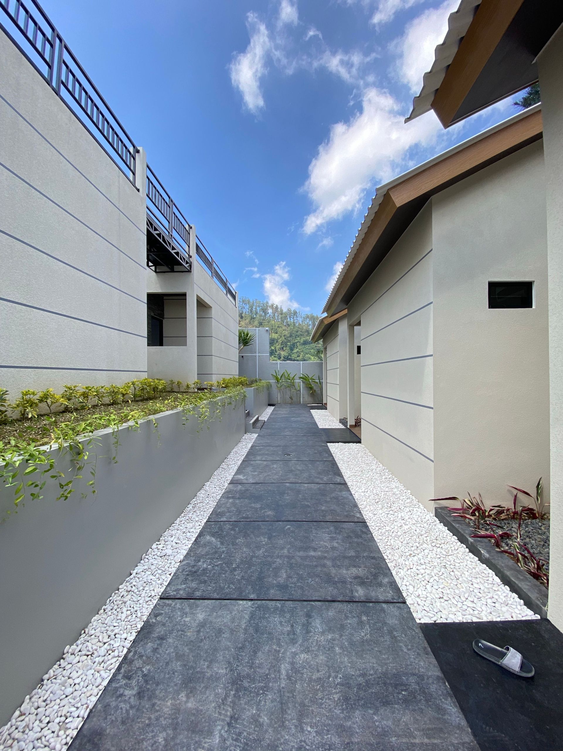A sleek, modern pathway with white stone borders between contemporary buildings under a clear blue sky.