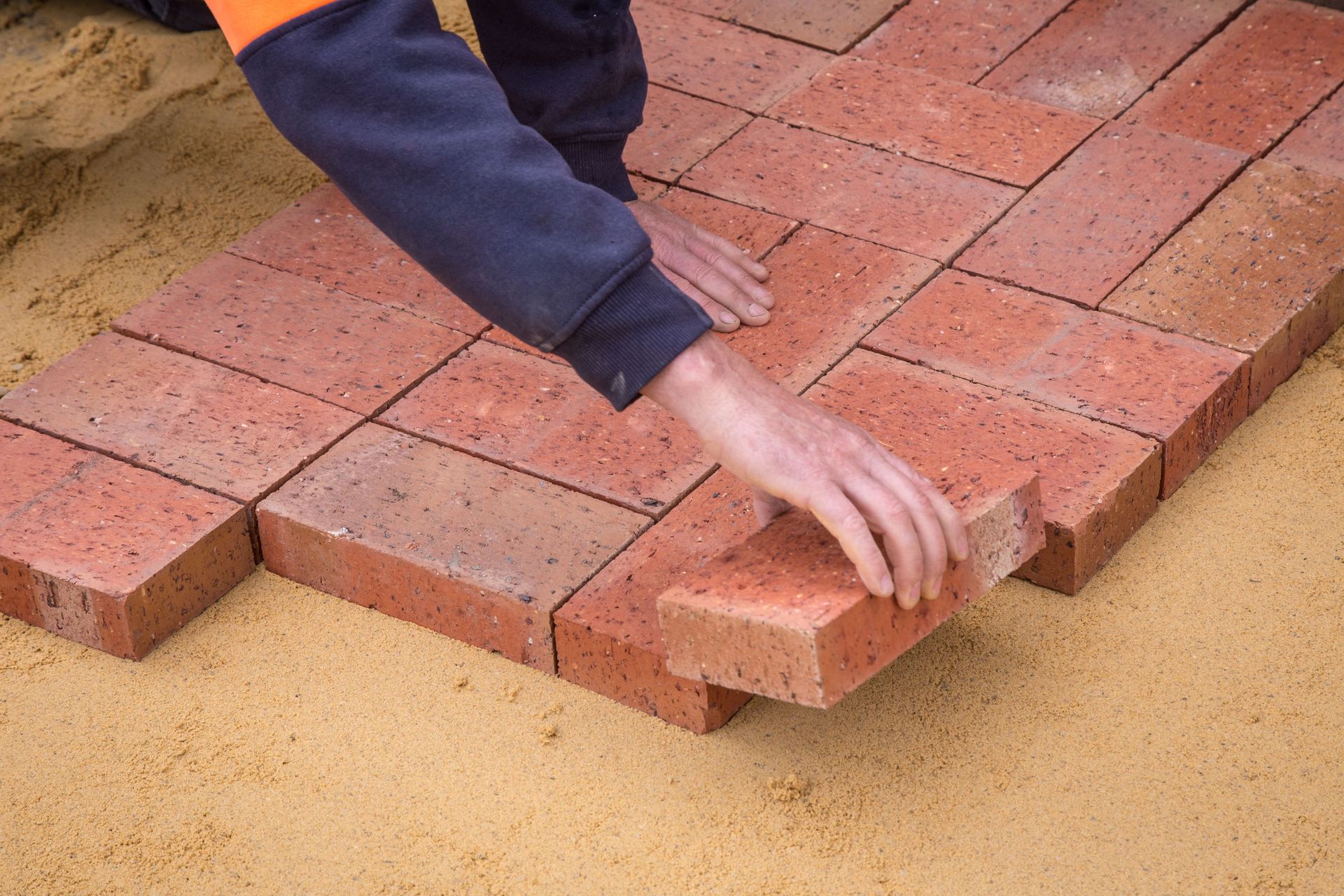 From above crop unrecognizable construction worker in uniform laying bricks on ground in daylight